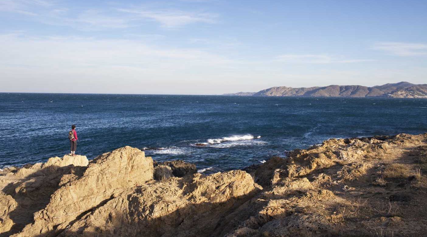 Nainen seisoo rantakivellä ja katselee merelle Cap de Creusin niemellä.