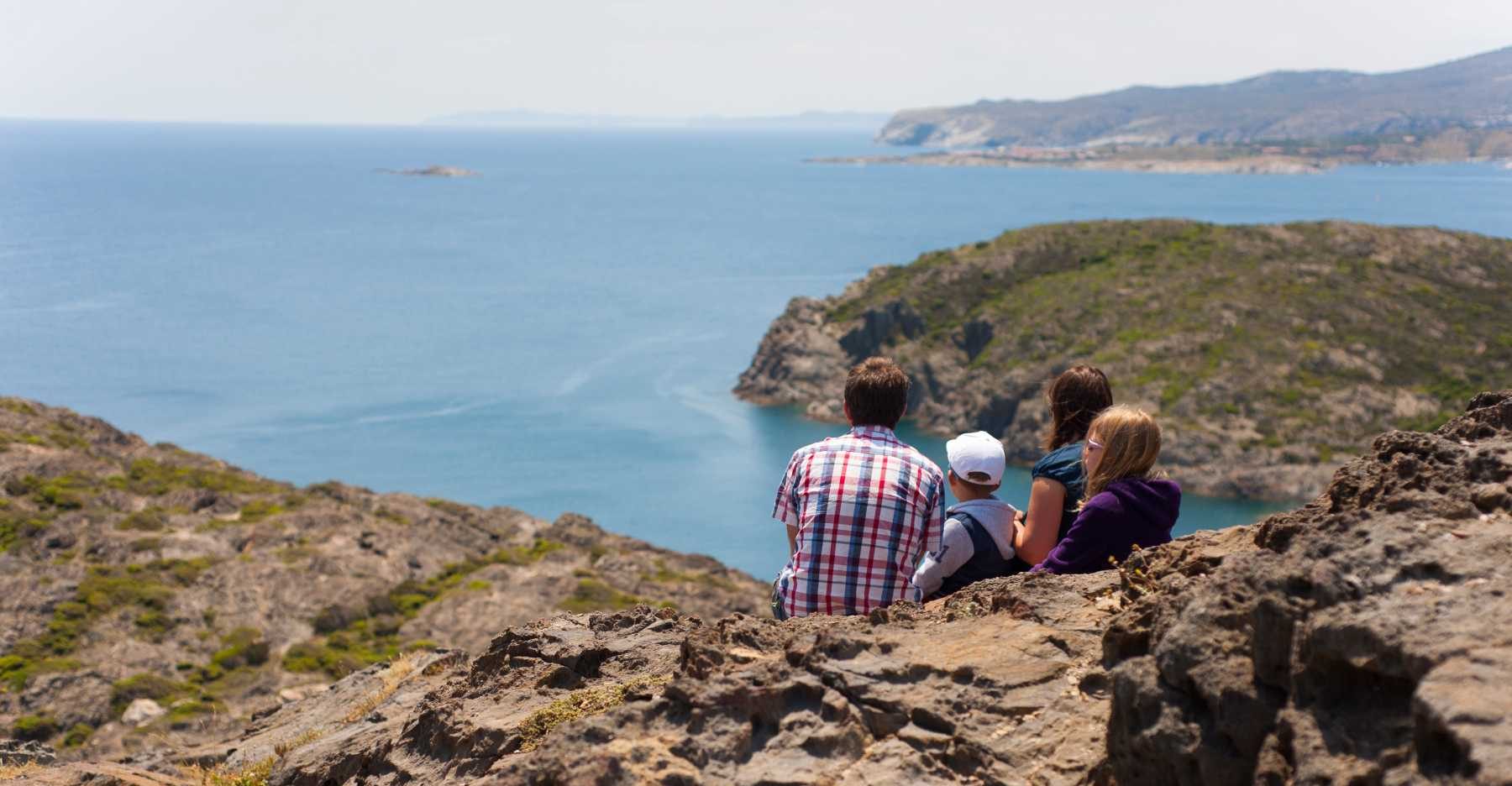 Perhe istuskelee rantakalliolla ja katselee merelle Cap de Creusin niemellä.