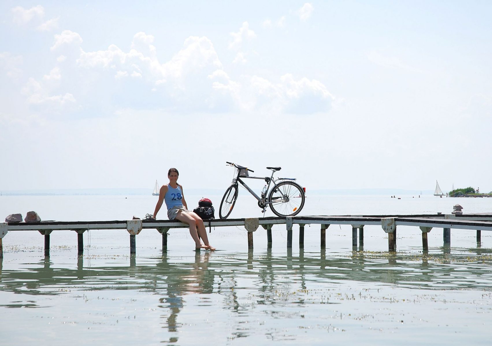 Nainen istuu laiturilla ja uittaa varpaita Balatonjärvessä.