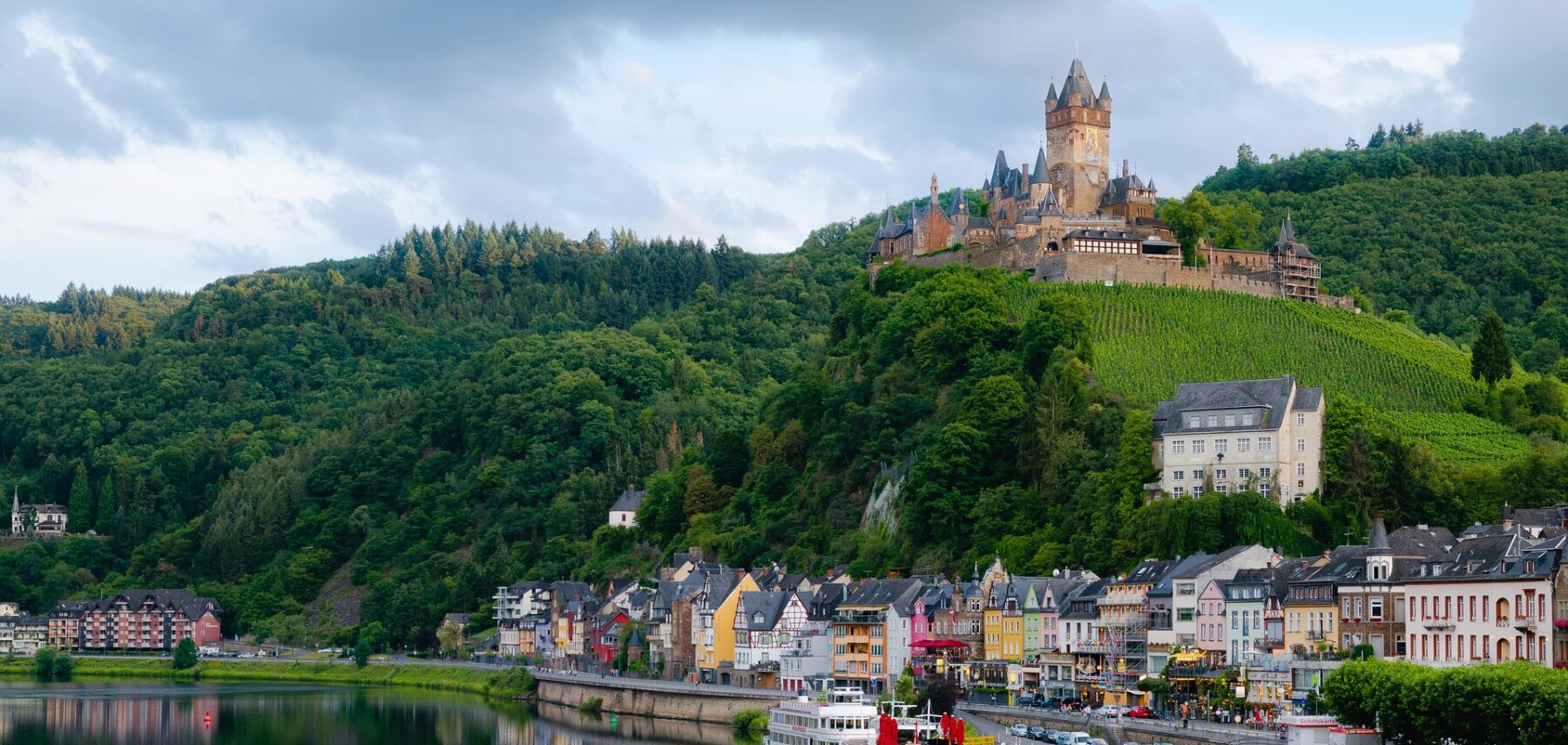 Värikkäitä taloja jokivarressa ja linna korkealla kukkulalla kylän yläpuolella.