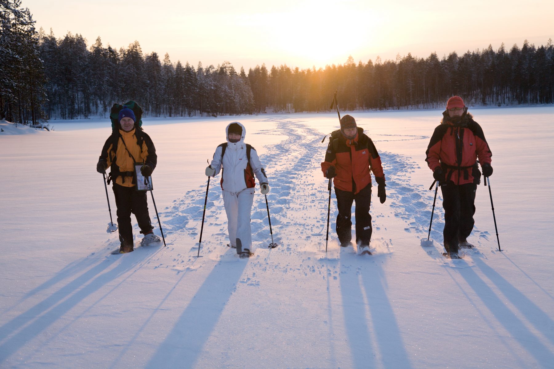 Neljä lumikenkäilijää järven jäällä tammikuun hennossa auringonpaisteessa.