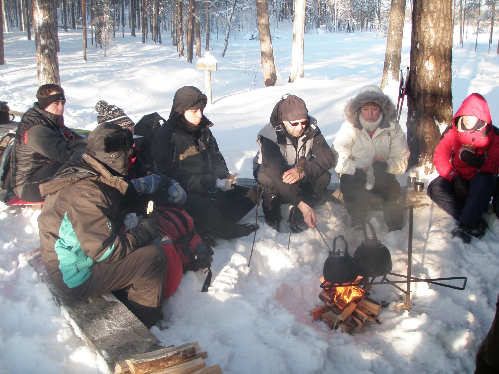 Retkeilijät lounastauolla nuotion ympärillä, missä kahvit ovat tulilla.