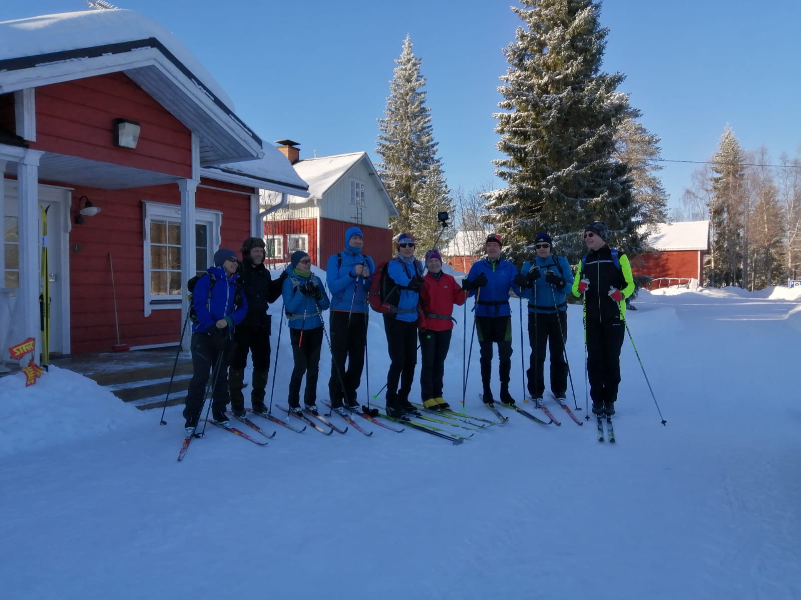 Ryhmä hiihtäjiä poseeraa majatalon edessä