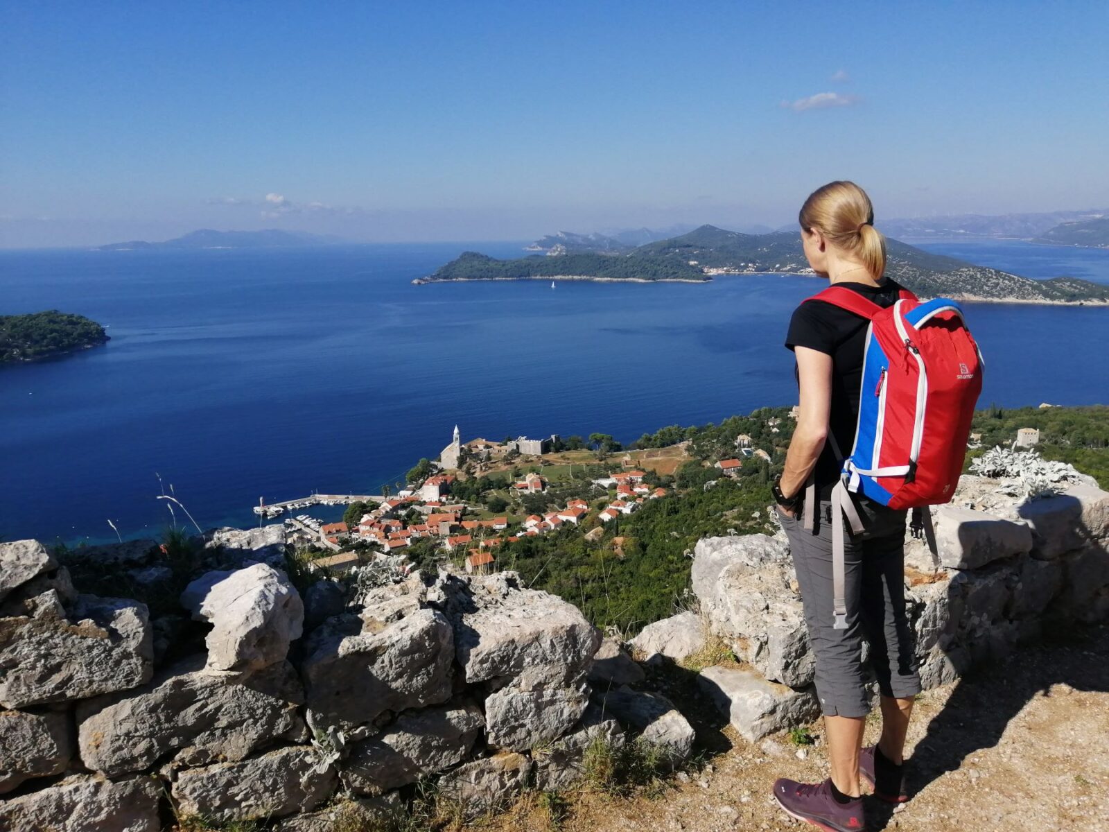 Nainen reppu selässä katselee merelle ylhäältä kukkulalta.