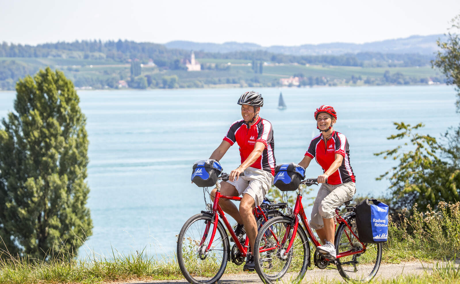 Pariskunta punaisissa paidoissaan pyöräilee rannan tuntumassa