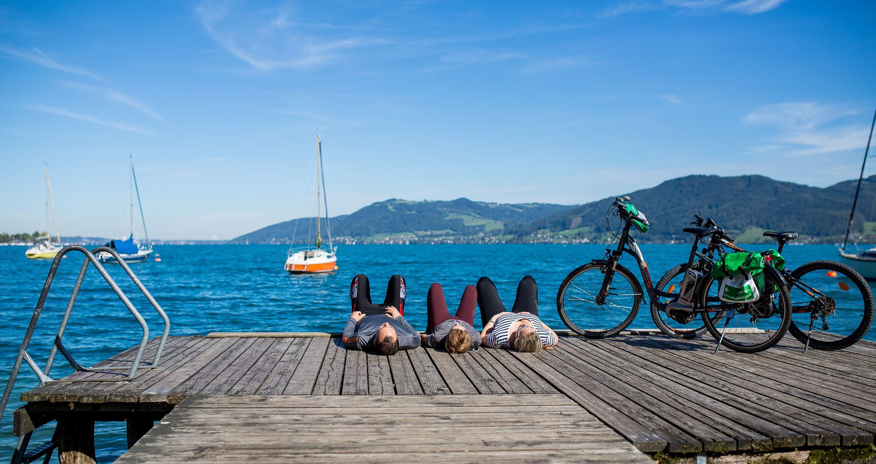 Kolme pyöräilijää rentoutuu laiturilla selällään maaten.
